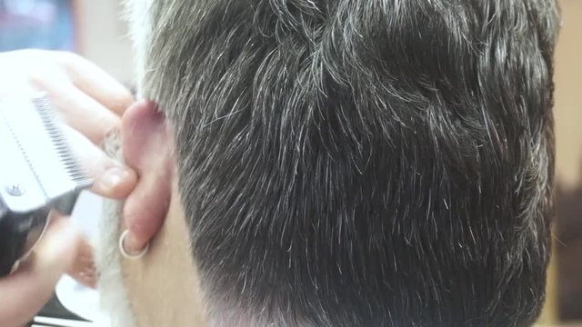 Close up barber cuts the hair of a senior man in the Barbershop
