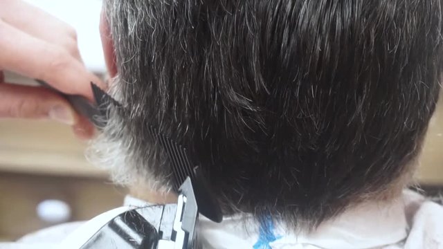 Close up barber cuts the hair of a senior man in the Barbershop