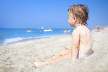 Fototapeta na wymiar Little child on sandy beach of sea looking at waves. Child on the sea on clear sunny day. Relax on the beach with children. Kid on white sand on the beach.