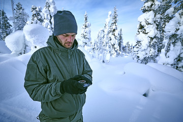 Fototapeta na wymiar Young man in military clothes is looking for way in the winter tundra forest with compass