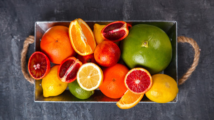 Different Citrus Fruit in a Metal tray on Gray Background .Mixed Colorful Tropical Background.Food or Healthy diet concept.Vegetarian.Copy space for Text. selective focus.