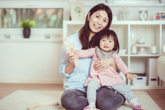 Pretty japanese woman playing with her cute laughing baby girl on the floor