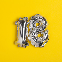 Silver foil number 18 celebration balloon on a bright yellow background