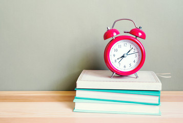 Red alarm clock  shows time 08:07 and books on a wooden surface of a table. School background