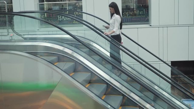 Young businesswoman portrait talking at the phone on escalators. Business woman full lenght in shopping mall or office building or airport terminal.