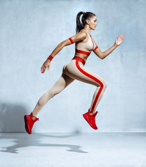 Sporty woman runner in fashionable sportswear on grey background. Dynamic movement. Side view