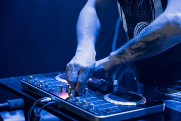 DJ work in a nightclub. Disco light in the club. DJ behind the turntable.