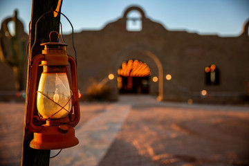 Old fashioned red Lantern hanging from post with adobe stucco building in background in desert.