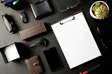 Top view of office desk with mock-up paper, eyeglass, pen, smartphone, key, wallet, agenda, cactus, stapler, Bluetooth audio headset, notes block