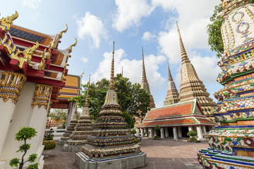 Buildings and many ornate chedis at the Wat Pho (Po) temple complex's courtyard in Bangkok, Thailand, on a sunny day.