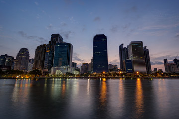 Fototapeta na wymiar View of modern skyscrapers behind a lake at the Benjakiti (Benjakitti) Park in Bangkok, Thailand, at dawn.