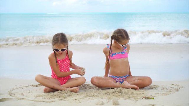 Adorable little girls playing with sand on the beach. Kids sitting in shallow water and making a sand castle