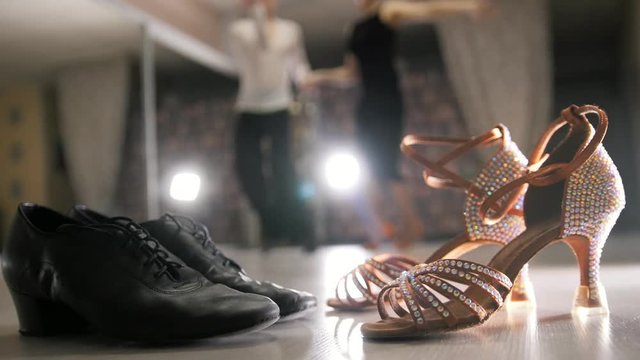Blurred professional man and woman dancing Latin dance in costumes in studio, two pairs ballroom shoes in the foreground
