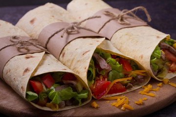 Tortilla, burritos, sandwiches twisted rolls. Wraps with beef, tomatoes, lettuce, cucumbers, cheddar cheese, corn and onion rings. horizontal