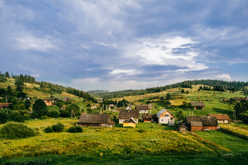 Fototapeta na wymiar Countryside rural nature landscape in summer sunny day. Discover Ukraine. Village in Carpathians mountains. Beautiful scenic view at green hills and rustic terrain. Farmer houses in forest territory.