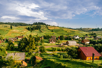 Countryside rural nature landscape in summer sunny day. Discover Ukraine. Village in Carpathians mountains. Beautiful scenic view at green hills and rustic terrain. Farmer houses in forest territory.