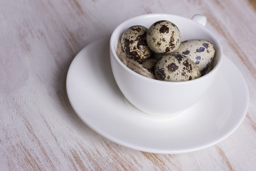 Quail eggs in a coffee cup and a bird nest with leaves on a white wooden background