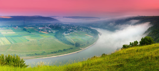 Panoramic view from the hill on bend of the river. Beautiful summer landscape. Colorful pink sky of the morning. Dniester Canyon located at the territory of Dniester River Valley in Ukraine.