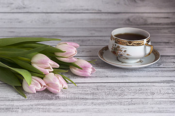 Bukiet różowych tulipanów na drewnianym stole z porcelanową filiżanką herbaty