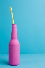 Pink bottle with cocktail straw on blue background, copy space. Cocktail, milkshake, drink concept.