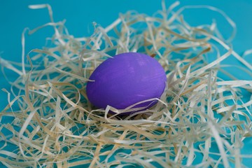 Violet Easter egg in hay on blue background, close up. Easter, spring, holidays, culture and religion concept
