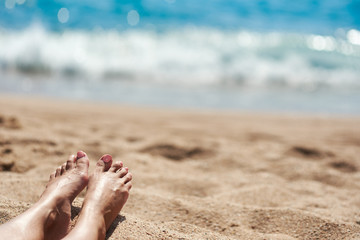 Female feet with manicured nails on the beach against the sea.