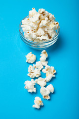 Popcorn in a glass bowl on a blue background.
