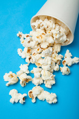 White popcorn scattered from a white paper bucket on a blue background.