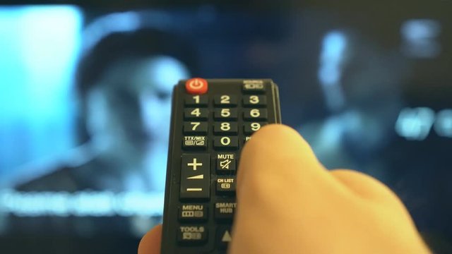Male hand switching channels on TV with remote control.