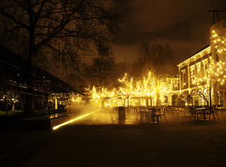 empty night restaurant, lot of tables and chairs with noone, magic fairy lights on trees like...