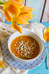 
Pumpkin, carrot and pepper soup. Blue wooden background. Orange tulip.