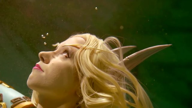 Close up shot of enchanting female elf swimming underwater alone. She is touching her blonde hairs.