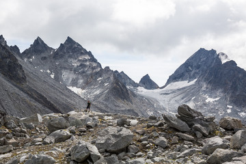Fototapeta na wymiar Man standing below huge cirque, glacier, and rocky peaks in the Talkeetna Mountains of Alaska