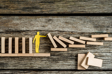 Single man holding up falling wooden bricks in a conceptual image