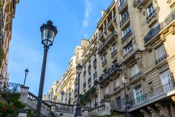 Low angle view of opulent-looking, Haussmannian style buildings in the chic neighborhoods of Paris, with period street lights in the foreground against blue sky.