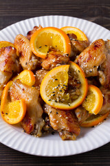 Sweet and sour chicken wings with oranges, served with sesame on white plate