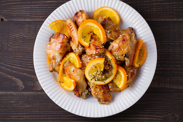Sweet and sour chicken wings with oranges, served with sesame on white plate