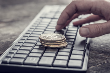 Golden Bitcoin coin over black computer keyboard and male fingers typing