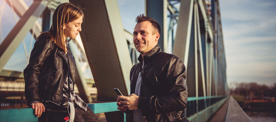 Father and daughter resting on the bridge and using smart phone