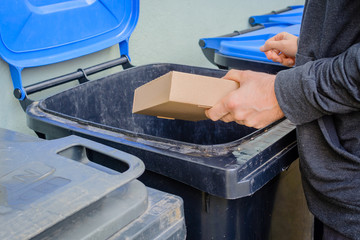 Men putting card paper box in blue garbage container