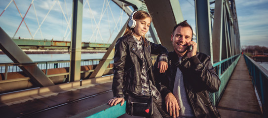Obraz na płótnie Canvas Father and daughter relaxing on bridge and listening music