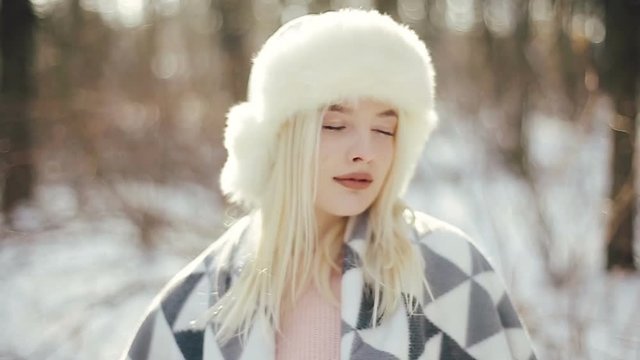 Close-up of a cute blonde woman with blue eyes in a winter forest poses on the camera and looks to the side