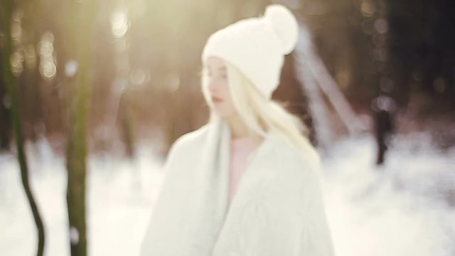 The camera slowly rolls to the young blonde girl in a white cap in the winter forest.