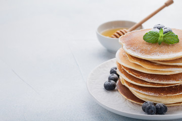 A stack of delicious pancakes with honey and blueberries on a light blue background. with copy space