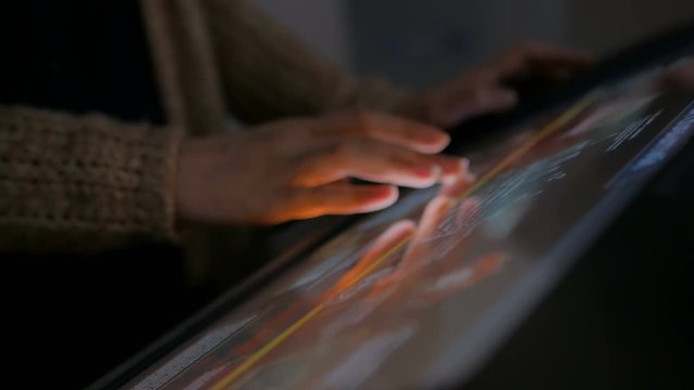 Woman using interactive touchscreen display in modern historical museum. Evening time, lowlight. Education and entertainment concept. Close up shot