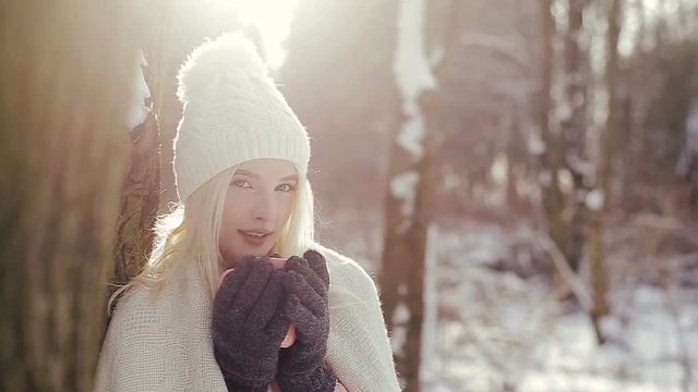 Close up of cute blonde girl with a warm blanket and pink cup in her hands in the winter forest.