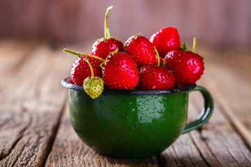 Fresh Strawberries in a Green enamel Cup on Vintage Wooden Background..Food or Healthy diet concept.Vegetarian.Copy space for Text. selective focus