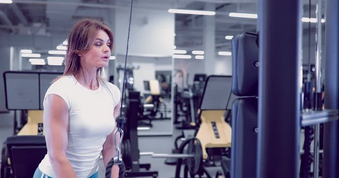 Adult woman doing Exercises for Tricep in fitness gym. Beautiful Woman doing triceps workout. Fitness girl doing triceps cable pushdown exercise in gym