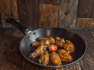 Chicken wings in a frying pan with fresh tomato