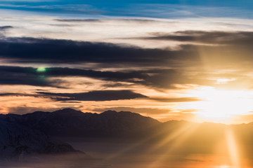 Utahs snow covered mountains from an airplane just as the sun starts to set. Thus creating an array of vibrant yellows and oranges while silhouetting the mountains.